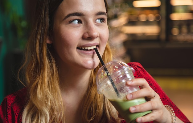 カフェで若い女性がグリーンドリンクアイスラテを飲む