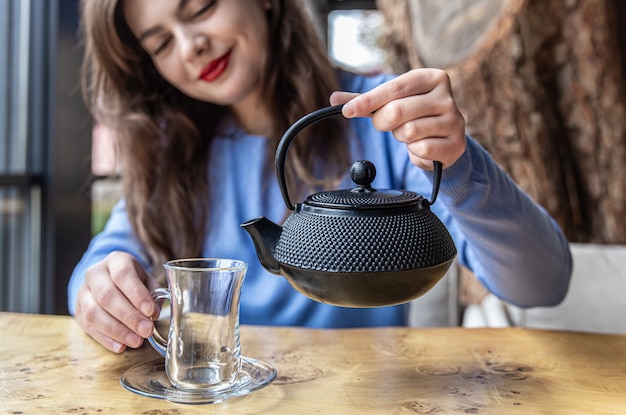 Young woman in a cafe pours tea from a black cast iron teapot