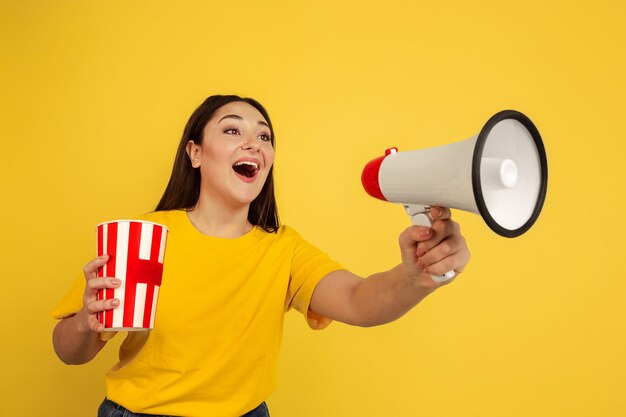 Young woman calling with megaphone and holding popcorn