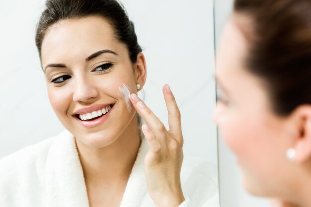 Young woman caring of her skin standing near mirror in the bathr