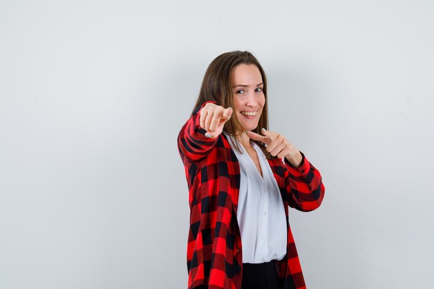 Young woman in casual clothes pointing at camera and looking jolly , front view.