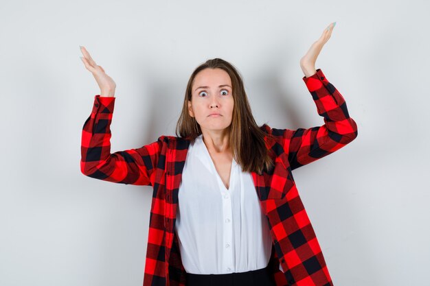 Young woman in casual clothes raising arms and hands and looking angry , front view.