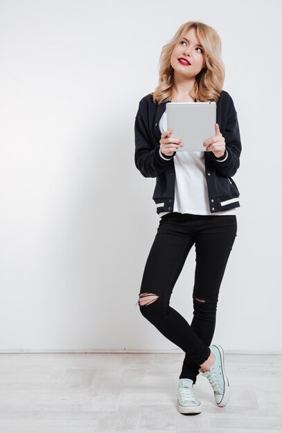 Young woman in casual clothes thinking and holding tablet computer