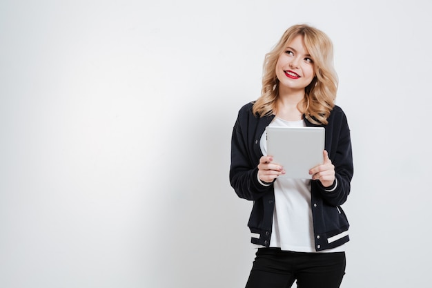 Young woman in casual clothes thinking and holding tablet computer