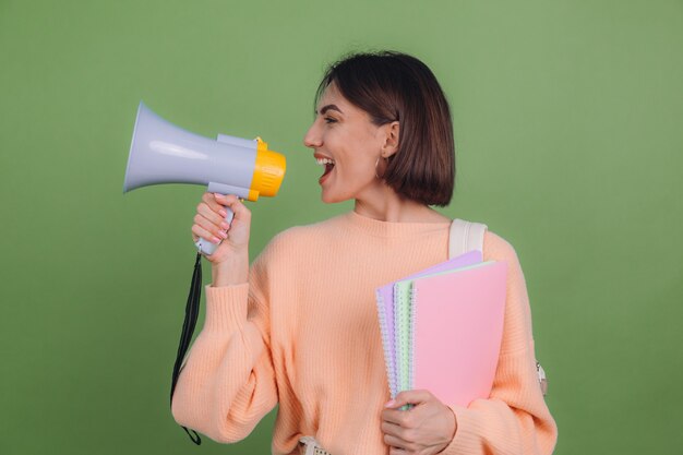 Young woman in casual peach sweater and backpack isolated on green olive color wall