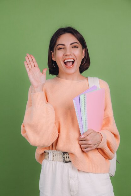 Young woman in casual peach sweater and backpack isolated on green olive color wall