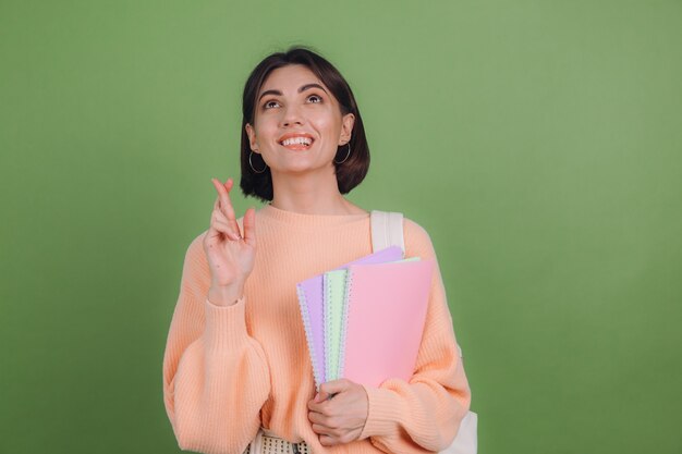 Young woman in casual peach sweater and backpack isolated on green olive color wall