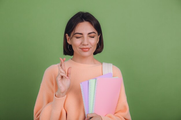 Young woman in casual peach sweater and backpack isolated on green olive color wall