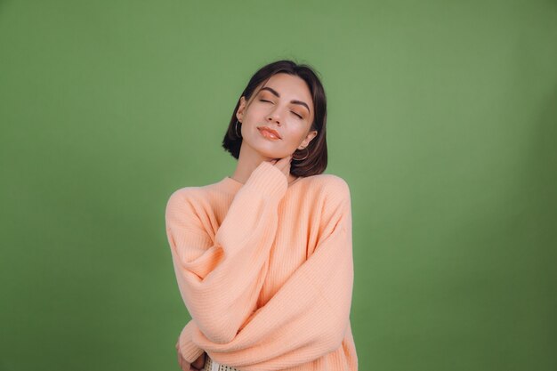 Young woman in casual peach sweater isolated on green olive color wall