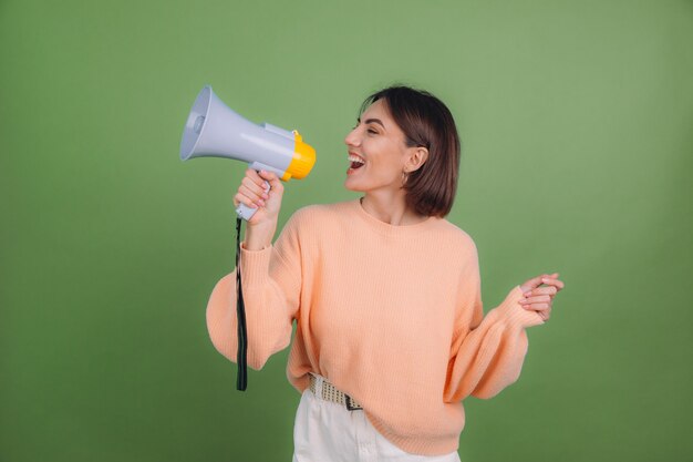 Young woman in casual peach sweater isolated on green olive color wall