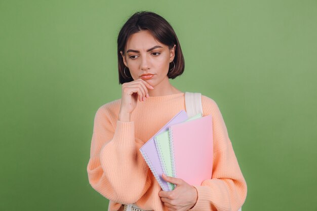 Young woman in casual peach sweater isolated on green olive color wall