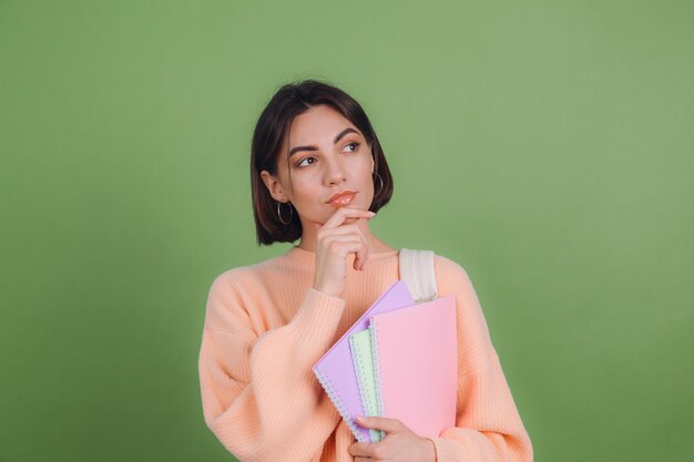 Молодая женщина в повседневном персиковом свитере изолирована на стене зеленого оливкового цвета