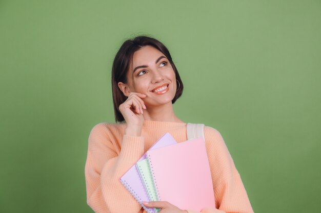 Young woman in casual peach sweater isolated on green olive color wall