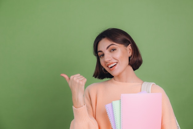 Young woman in casual peach sweater isolated on green olive color wall