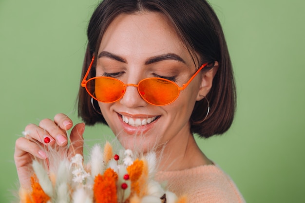 Young woman in casual peach sweater  isolated on green olive wall  hold  orange white flower box composition of cotton flowers, gypsophila, wheat and lagurus for a gift happy surprised