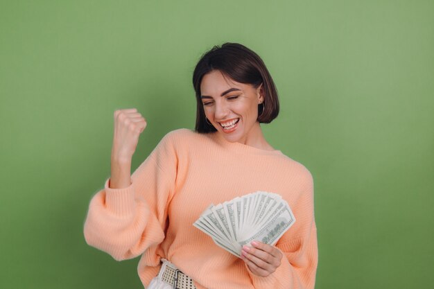 Young woman in casual peach sweater isolated on green olive wall