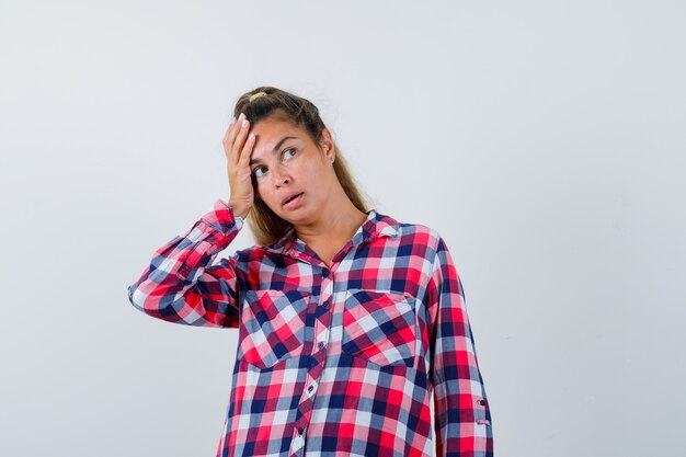 Young woman in casual shirt keeping hand on head and looking pensive , front view.