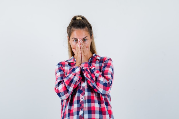 Free photo young woman in casual shirt keeping hands on face and looking agitated , front view.