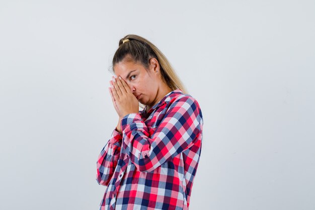 Young woman in casual shirt keeping hands in praying gesture and looking hopeful , front view.