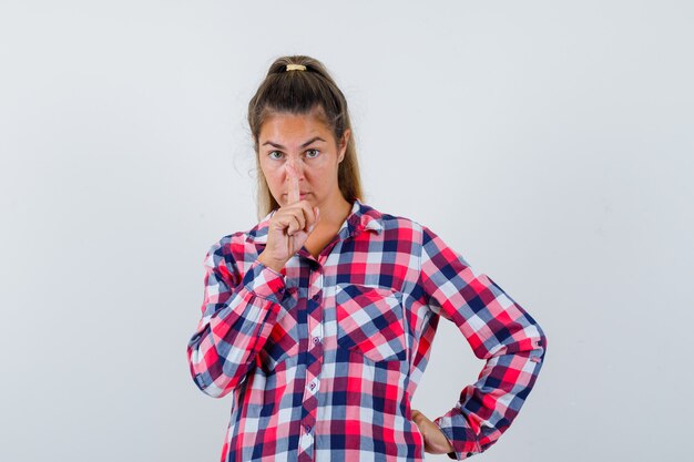 Young woman in casual shirt showing silence gesture and looking sensible , front view.