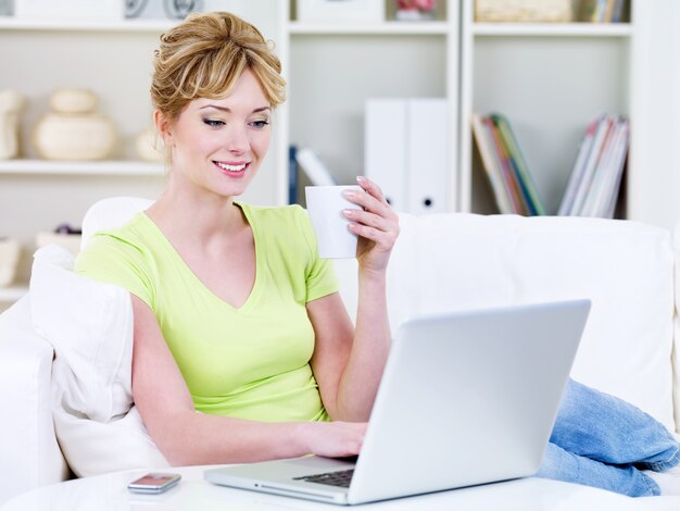 Young woman in casuals with cup of coffee and laptop in the sofa at home