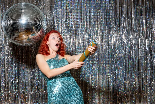 明るいカーテンでパーティーで爆竹を吹く新年を祝う若い女性