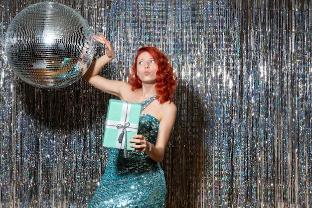 young woman celebrating new year holding present in party on bright curtains