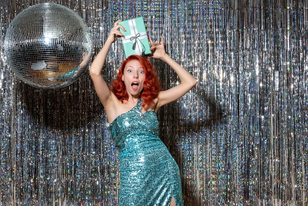 young woman celebrating new year holding present in party on bright curtains