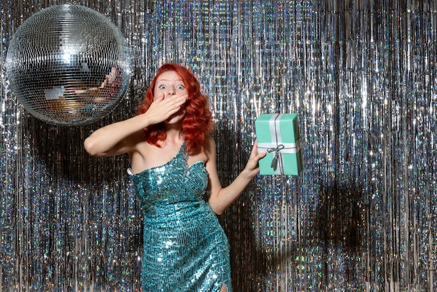 Free photo young woman celebrating new year holding present in party on bright curtains