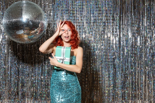 young woman celebrating new year holding present in party on bright curtains