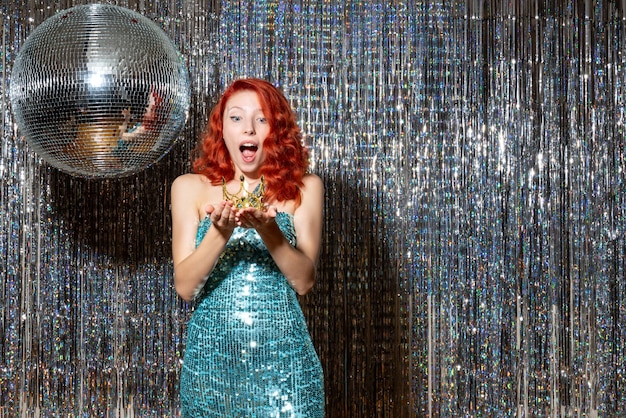 young woman celebrating new year in party holding crown on bright curtains