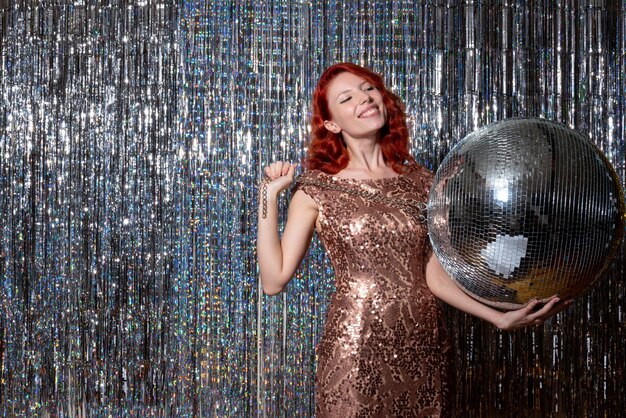 young woman celebrating new year in party holding disco ball on bright curtains curtains