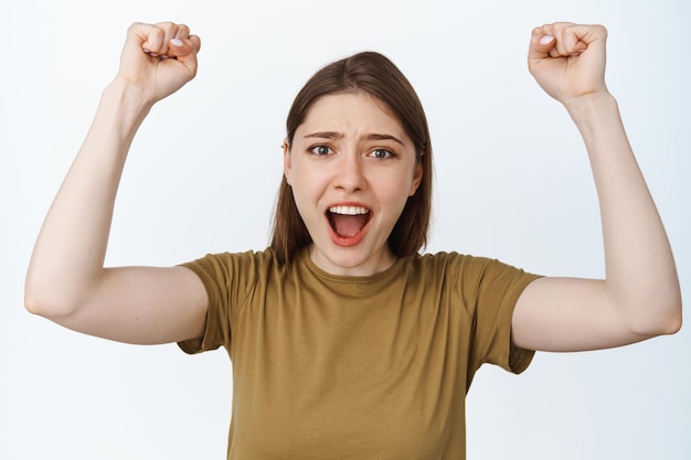 Young woman chanting, raising fists up and shouting to encourage you, watching sports game, rooting for team, standing against white background.