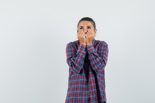 Young woman in checked shirt biting fists and looking happy , front view.