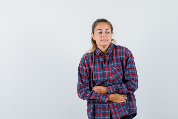 Young woman in checked shirt having bellyache and looking tired