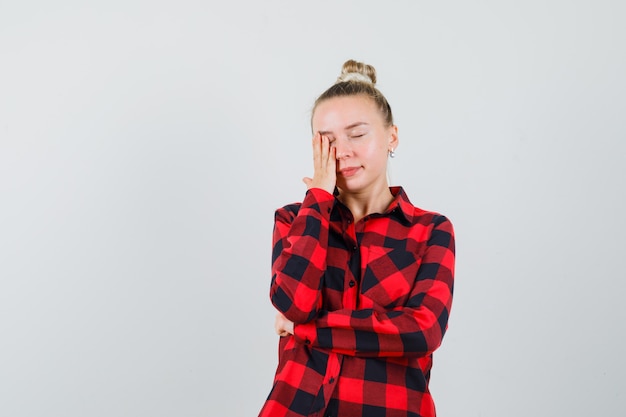 Young woman in checked shirt holding hand on face and looking peaceful