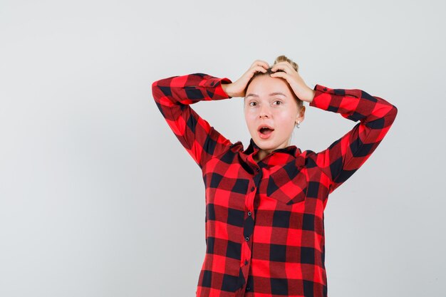 Young woman in checked shirt holding hands on head and looking frisky