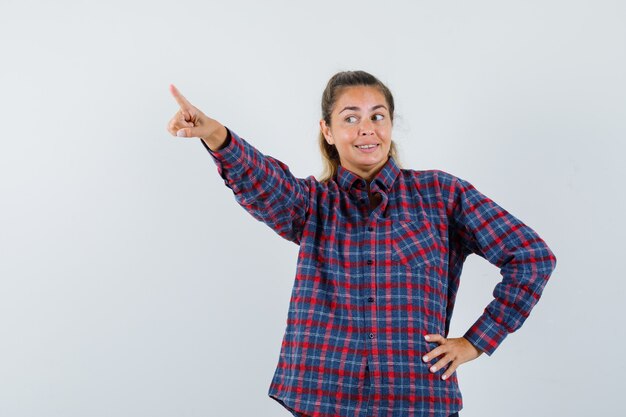 Young woman in checked shirt pointing away and looking pretty