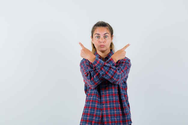 Young woman in checked shirt pointing at different directions and looking serious