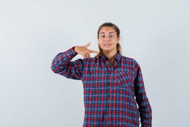 Young woman in checked shirt pointing at herself and looking pretty