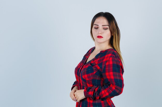 Young woman in checked shirt posing while looking down and looking attractive , front view.