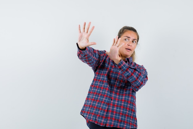 Foto gratuita giovane donna in camicia a quadri alzando le mani come cercando di fermare qualcosa e guardando spaventata