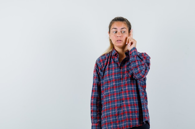 Free photo young woman in checked shirt raising index finger in eureka gesture and looking pensive