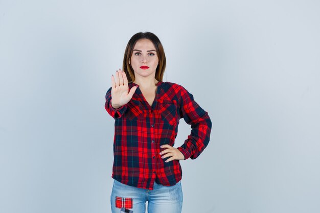 Young woman in checked shirt showing stop gesture and looking confident , front view.