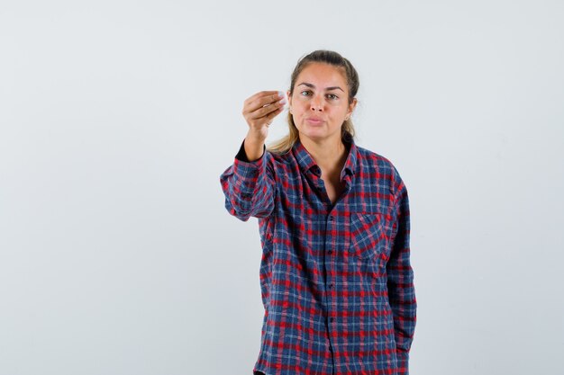 Young woman in checked shirt stretching hand as holding something and looking at it and looking focused