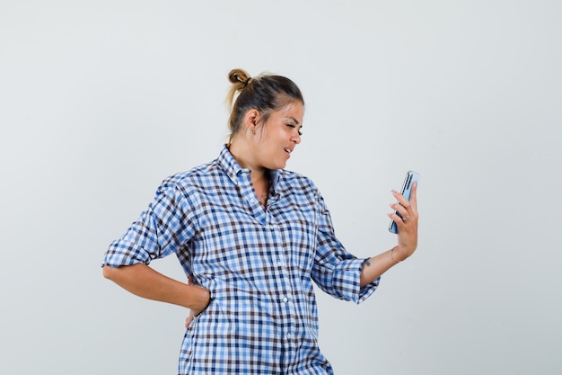 Young woman in checkered shirt making video call on phone.