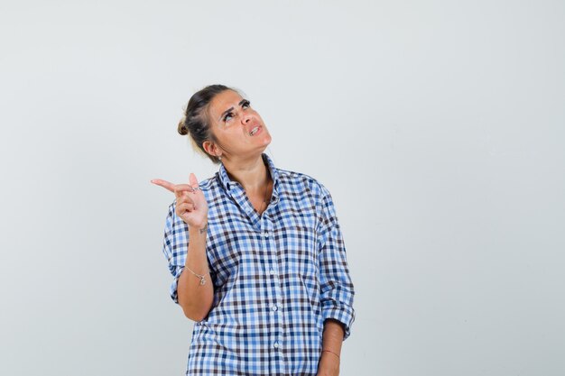 Young woman in checkered shirt pointing away and looking excited.