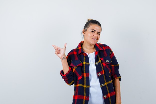 Young woman in checkered shirt pointing up and looking funny , front view.