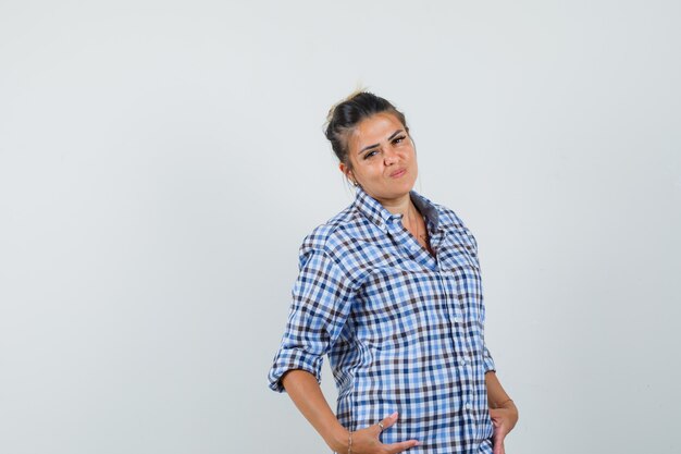 Young woman in checkered shirt posing and looking confident.