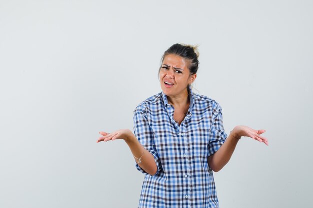 Young woman in checkered shirt showing helpless gesture and looking hopeless.